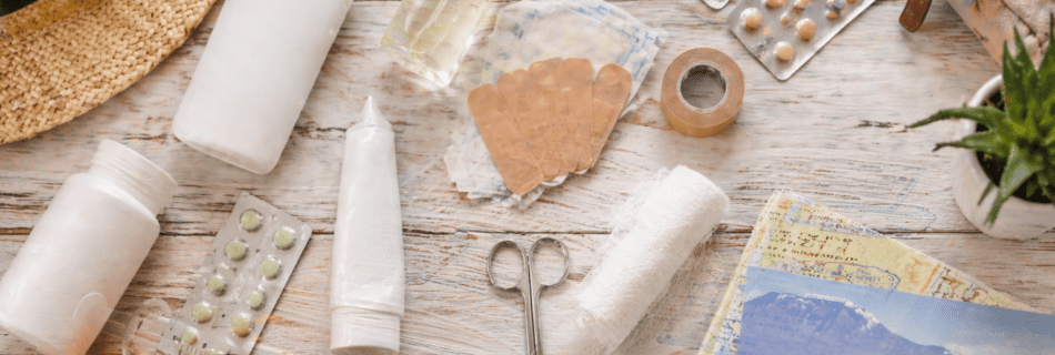 Reiseapotheke Südafrika mit Sonnencreme, Medikamenten und Verbandsmaterial auf Holzoberfläche