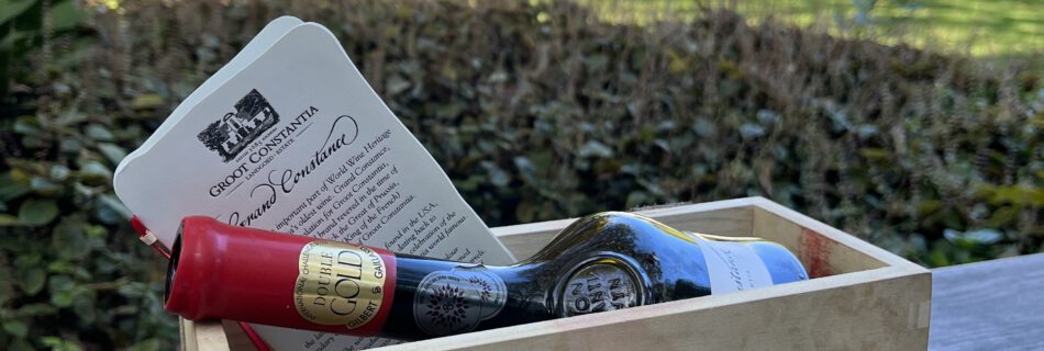 Holzkiste mit Groot Constantia Aufschrift und Grand Constance Weinflasche auf einem Holztisch im Garten